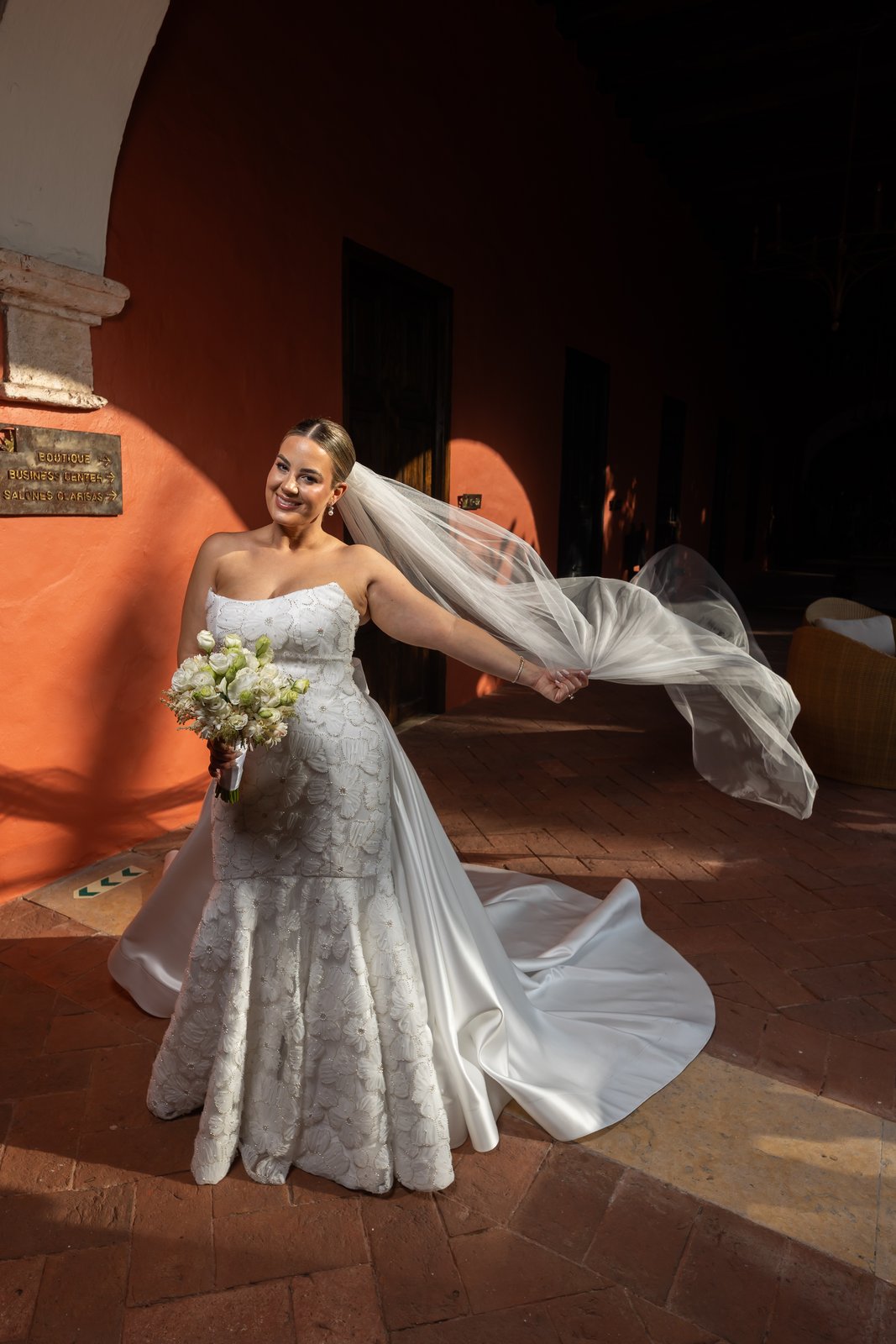 Novia con velo al aire frente a pared naranja en Cartagena