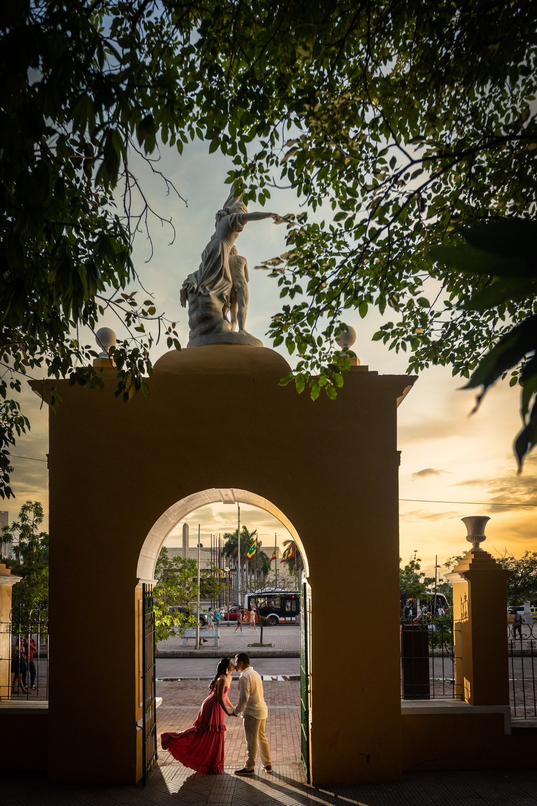 Pareja de novios bajo arco con estatua y atardecer dorado en Cartagena